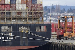A cargo container mover carries a container at right next to a cargo ship operated by Yang Ming Marine Transport Corp. at the Port of Tacoma, Friday, Feb. 20, 2015, in Tacoma, Wash.