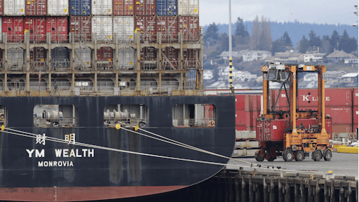 A cargo container mover carries a container at right next to a cargo ship operated by Yang Ming Marine Transport Corp. at the Port of Tacoma, Friday, Feb. 20, 2015, in Tacoma, Wash.