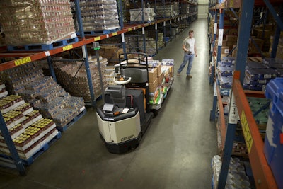 A warehouse worker uses Crown's QuickPick Remote to move the lift truck ahead in the aisle, eliminating the need to step up and down off the truck to move to the next pick position.