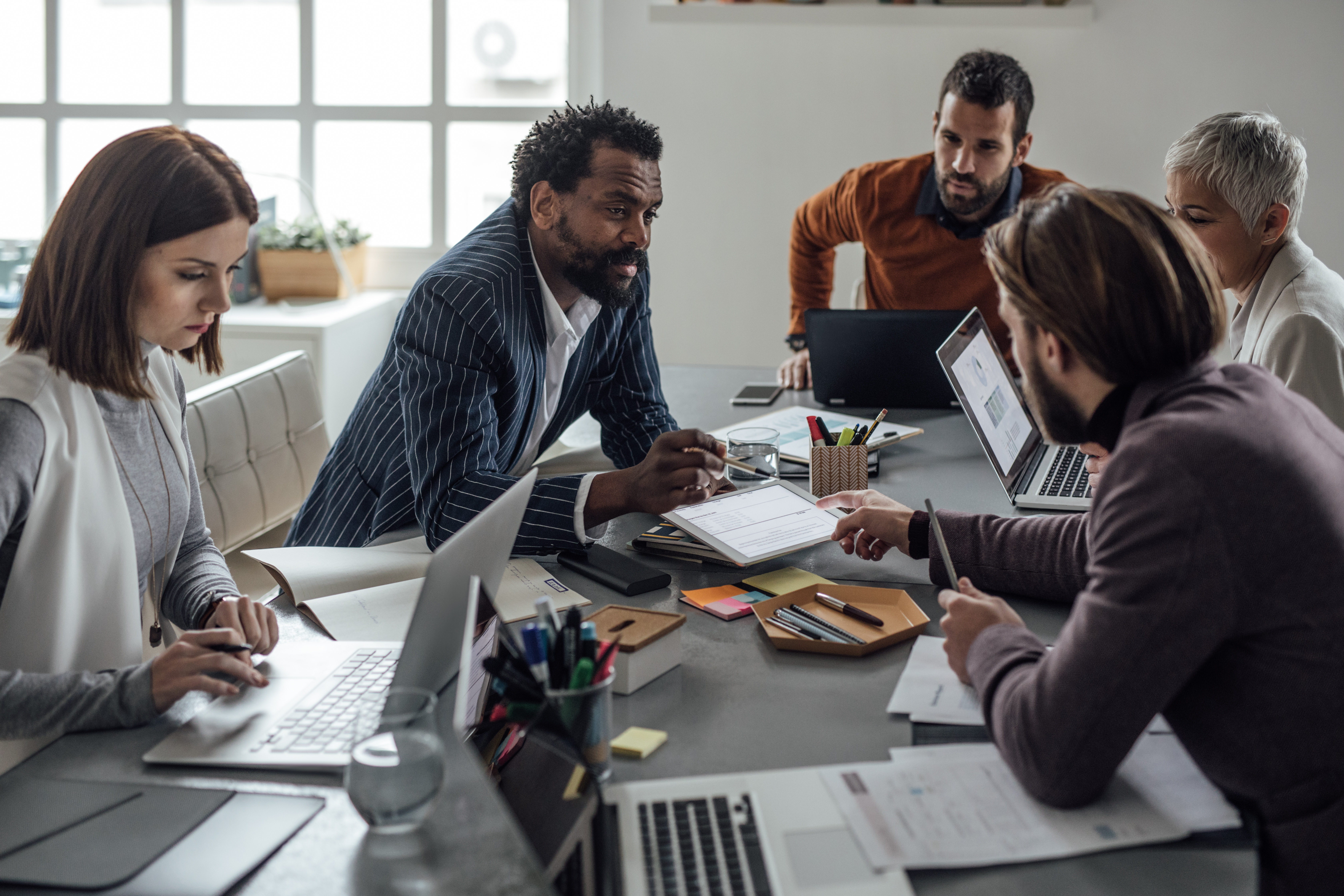 Diverse team of professionals collaborating during a business meeting at a conference table with laptops and documents.
