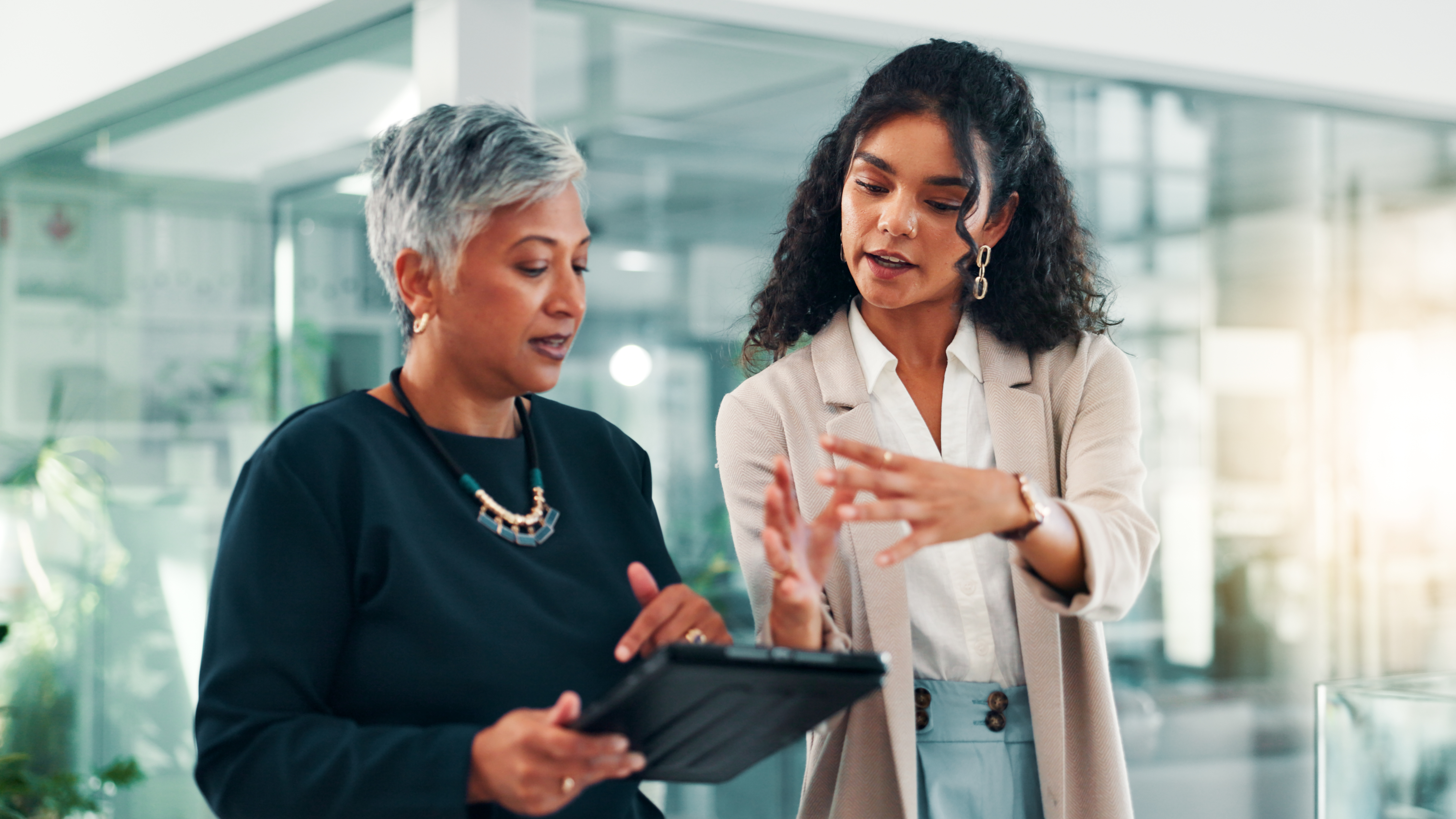 Two professional women discussing business strategy in a modern glass office environment