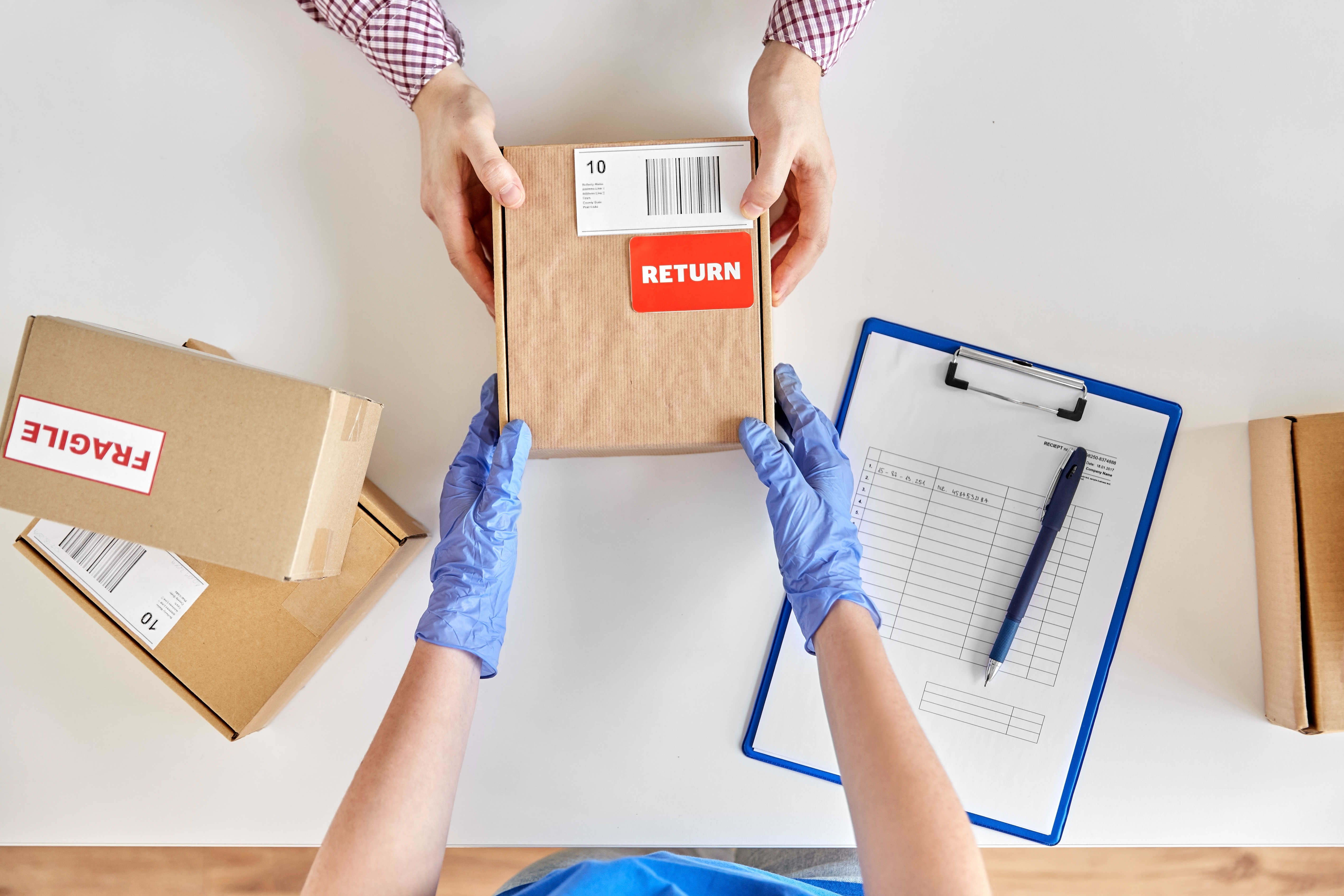 Person processing package return with red label, clipboard, and shipping boxes on white surface