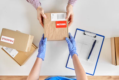 Person processing package return with red label, clipboard, and shipping boxes on white surface