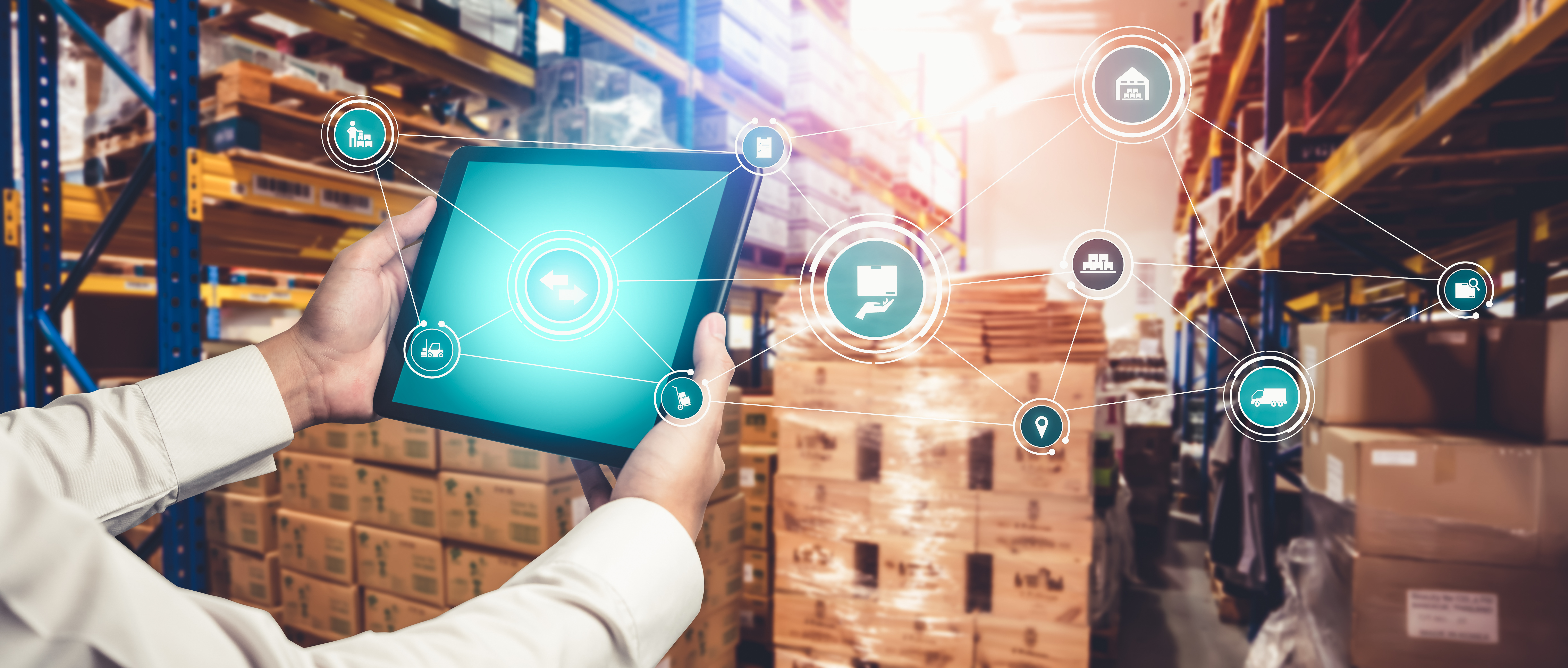 Worker holding tablet with digital logistics icons in warehouse with stacked boxes