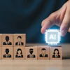 Hand placing glowing AI chip icon among wooden blocks with business professional silhouettes representing artificial intelligence in workforce management