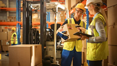 Warehouse workers in safety gear inspect a cardboard box near a forklift in a logistics facility.