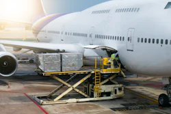 Cargo containers being loaded onto a large commercial aircraft at an airport using yellow ground support equipment.