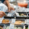 Chef preparing food at a catering station with multiple labeled dishes in metal containers