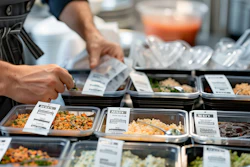 Chef preparing food at a catering station with multiple labeled dishes in metal containers