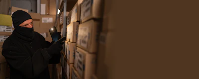 Person in dark winter gear examining cardboard boxes in warehouse storage facility