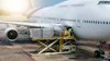 Cargo loader transferring freight containers to wide-body aircraft at airport during daytime operations