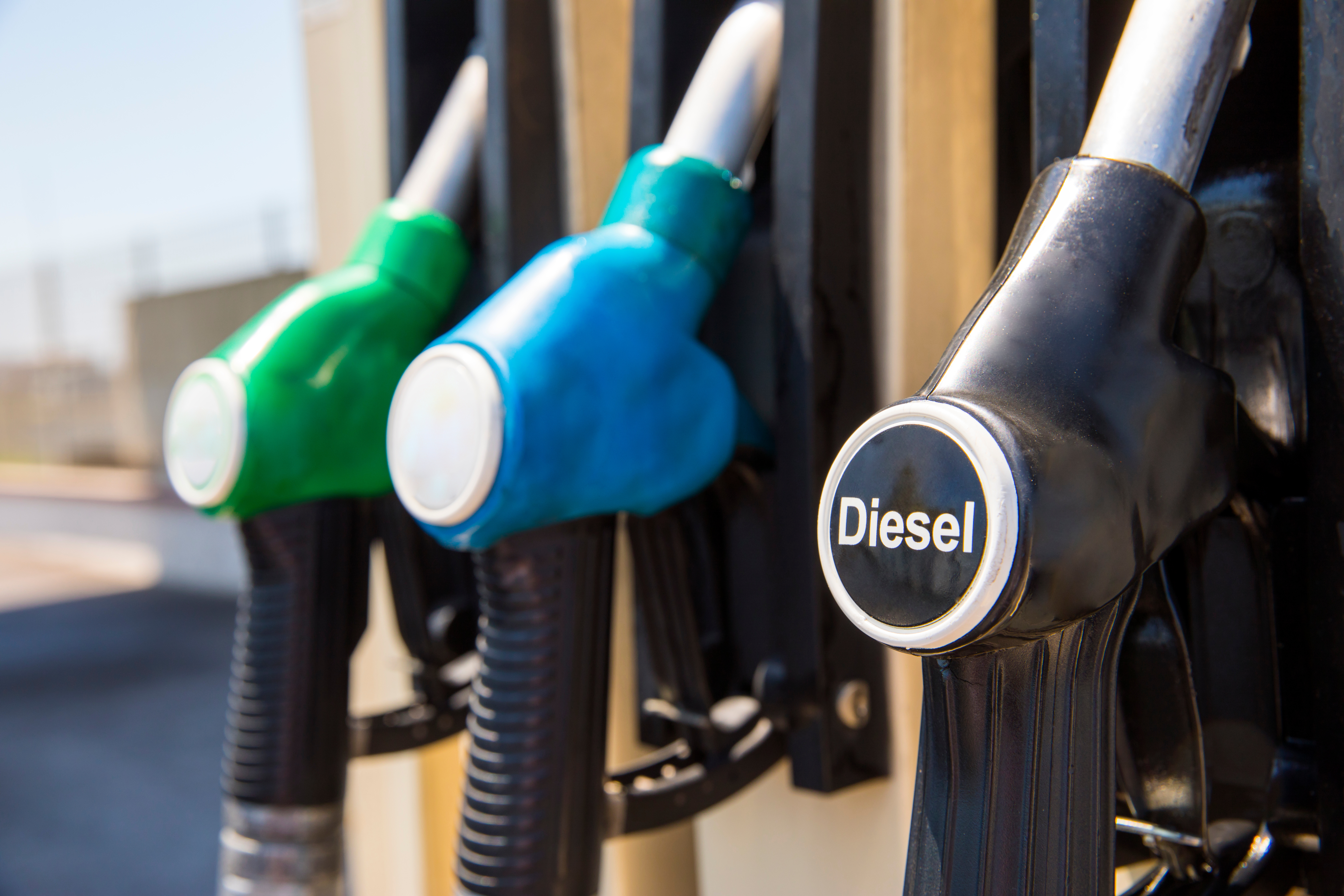 Fuel pump nozzles at gas station displaying green, blue, and black handles with Diesel label on the rightmost pump