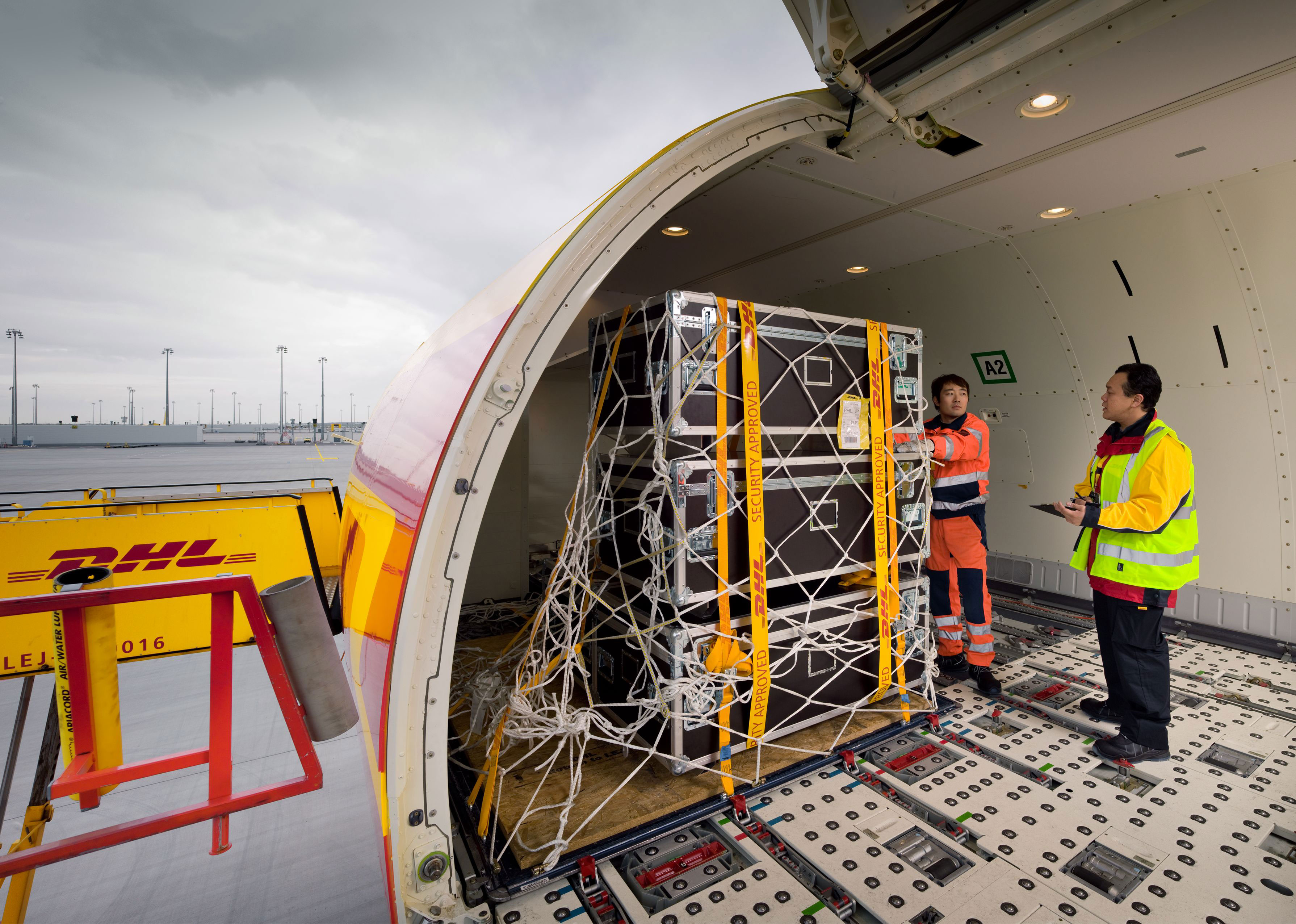 DHL cargo container being loaded into aircraft by workers in safety vests at airport terminal
