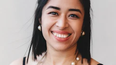 Professional headshot of smiling woman with dark hair wearing black top and pearl necklace