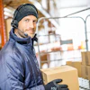 Warehouse worker wearing headphones and winter gear handling cardboard boxes in a logistics facility