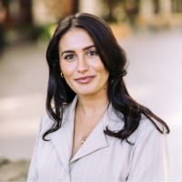 Professional headshot of woman with dark wavy hair wearing light gray blazer