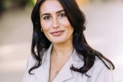 Professional headshot of woman with dark wavy hair wearing light gray blazer