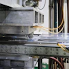 Industrial CNC machine or 3D printer with metal frame, control panel buttons, and yellow wiring in workshop setting