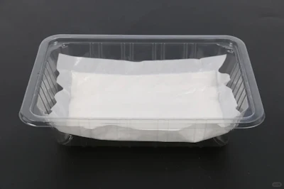 Empty clear plastic food container with white paper insert on dark background