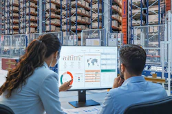 Two professionals reviewing analytics dashboards on a monitor in a warehouse with storage racks in the background