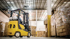 Yellow Yale forklift moving cardboard boxes in a warehouse with stacked pallets and industrial ceiling