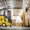 Yellow Yale forklift moving cardboard boxes in a warehouse with stacked pallets and industrial ceiling