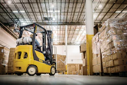 Yellow Yale forklift moving cardboard boxes in a warehouse with stacked pallets and industrial ceiling
