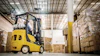 Yellow Yale forklift moving cardboard boxes in a warehouse with stacked pallets and industrial ceiling