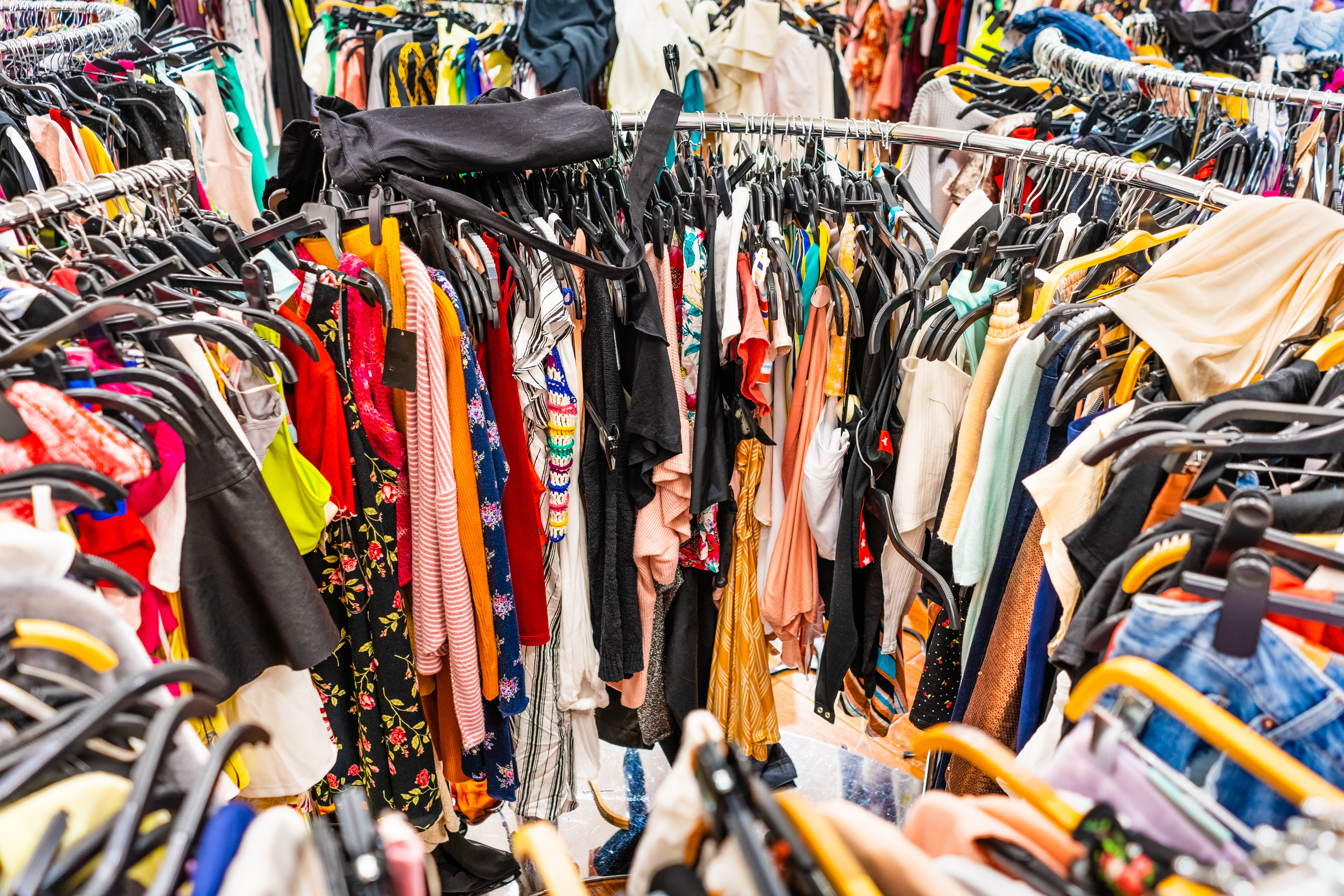 Crowded thrift store clothing rack with colorful garments on wooden hangers