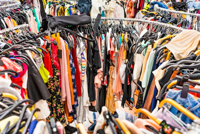 Crowded thrift store clothing rack with colorful garments on wooden hangers