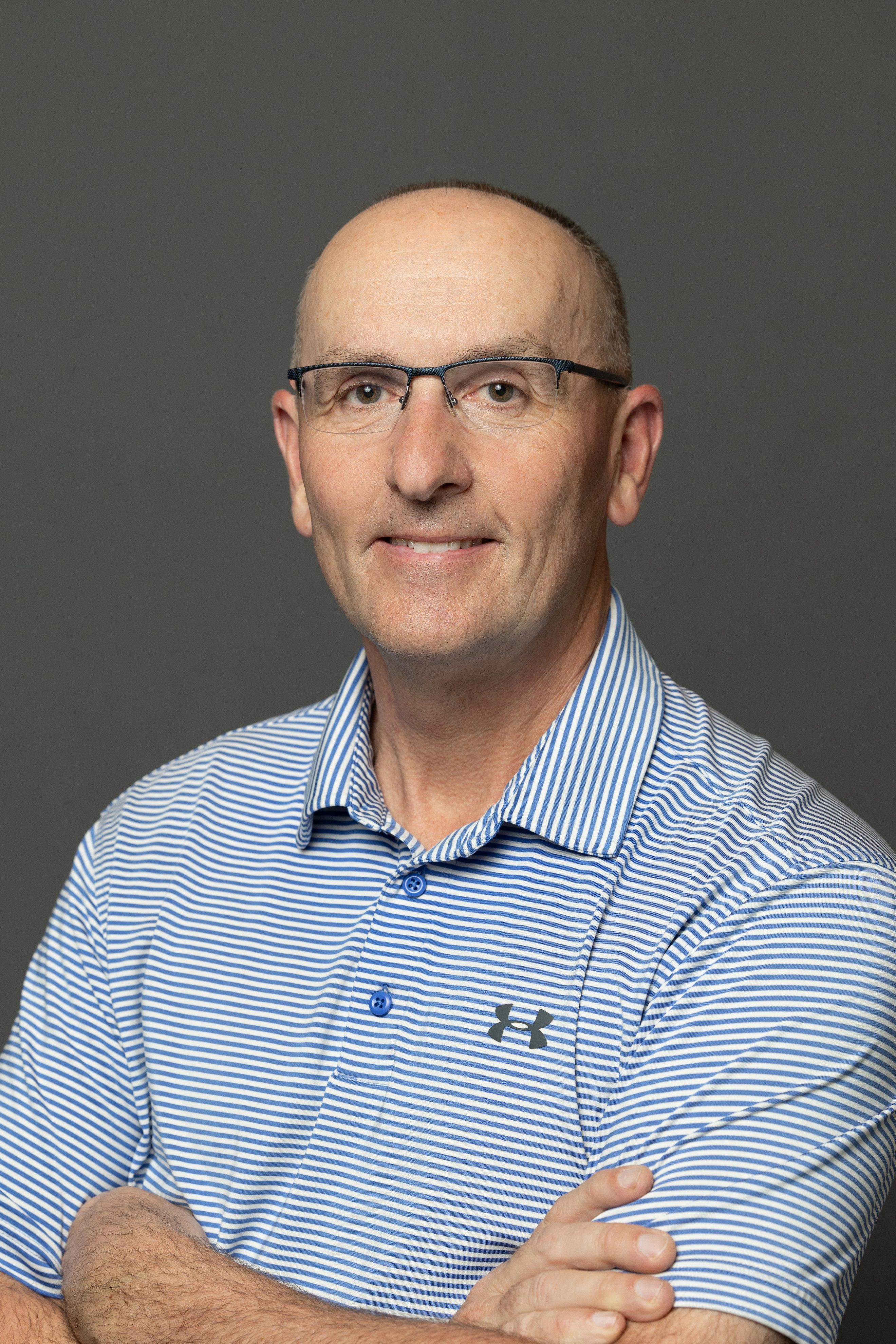 Professional headshot of man wearing blue striped polo shirt and glasses against gray background Headshot