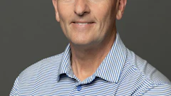 Professional headshot of man wearing blue striped polo shirt and glasses against gray background