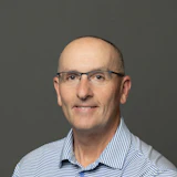 Professional headshot of man wearing blue striped polo shirt and glasses against gray background