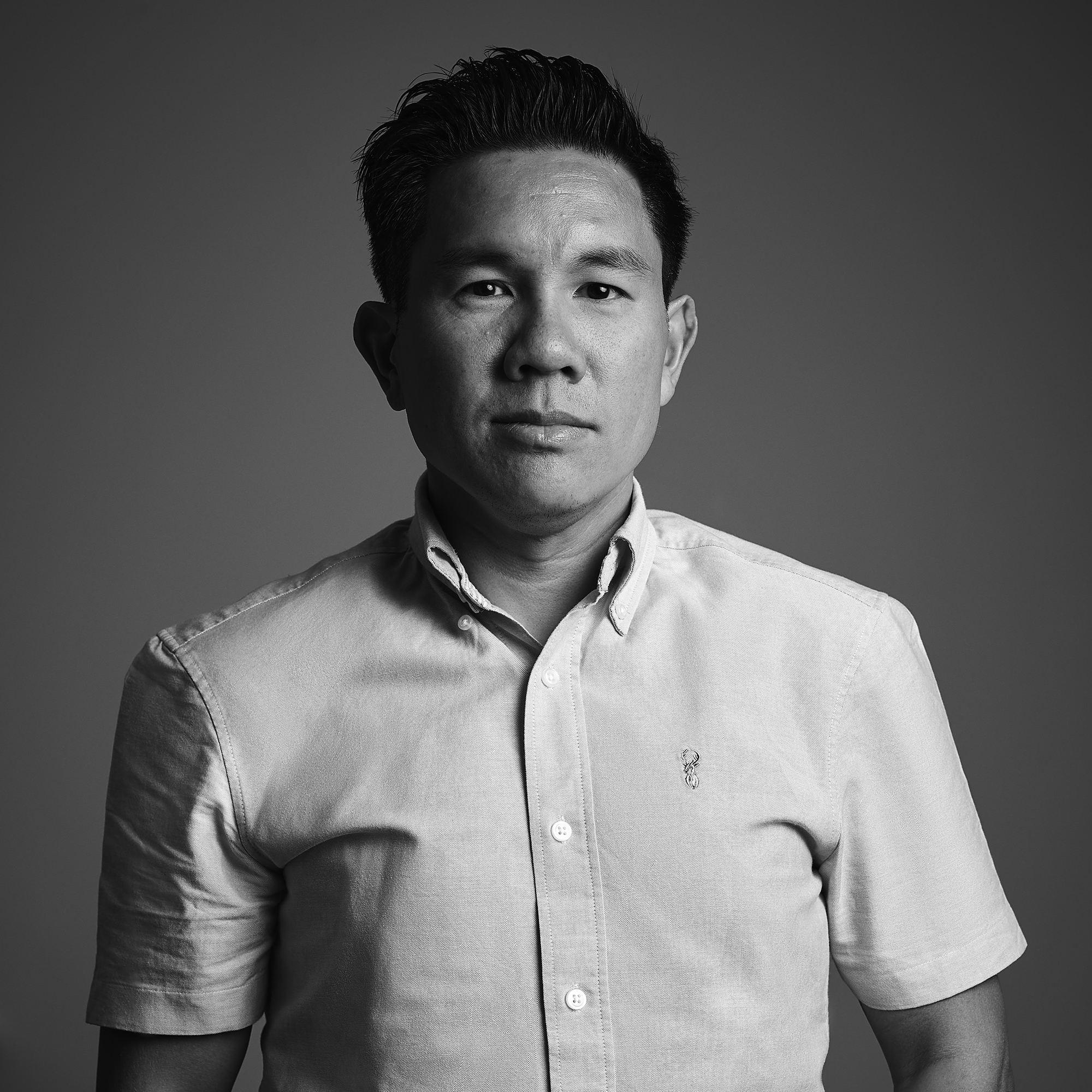 Professional black and white portrait of an Asian man wearing a light-colored button-up shirt against a neutral gray background