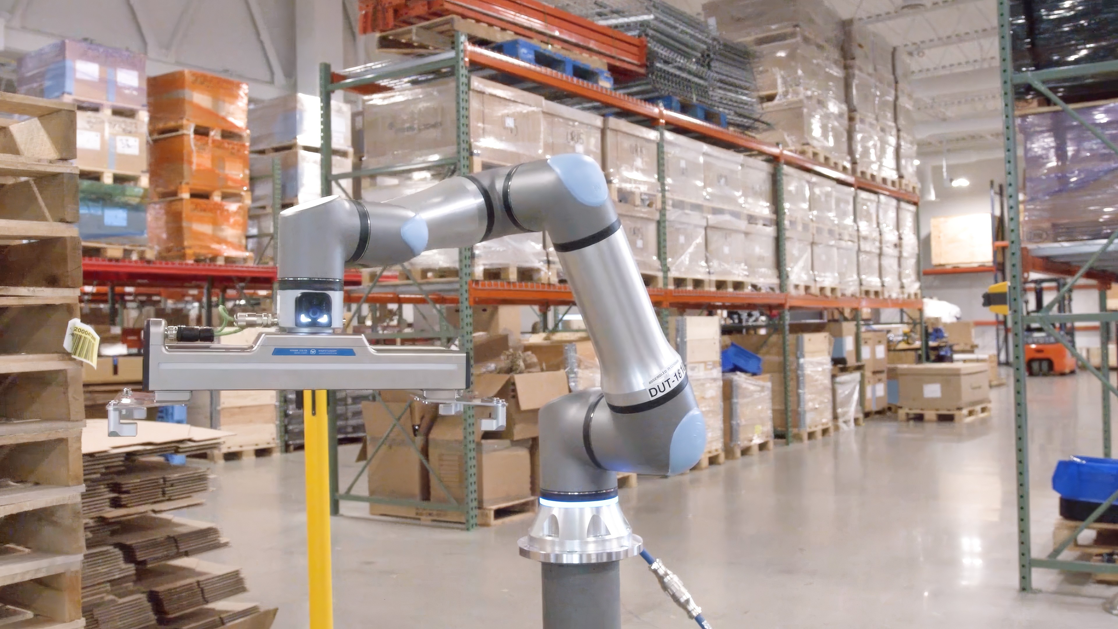 Collaborative robotic arm operating in an industrial warehouse with shelving and inventory.