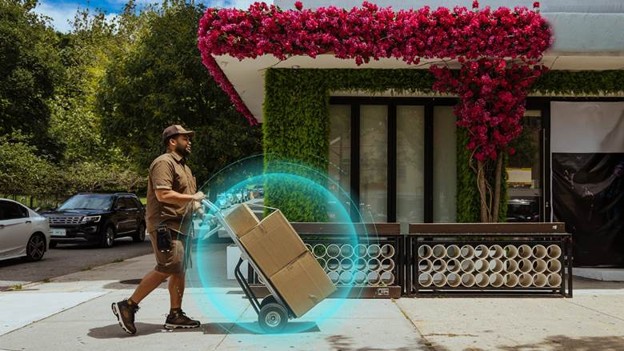 Delivery worker pushing hand truck with package outside modern storefront with red flowering vines and digital AR visualization effect