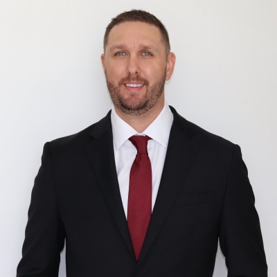 Professional headshot of a man in black blazer and burgundy tie against white background
