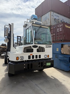 White industrial forklift with blue cabin parked in warehouse with shipping containers