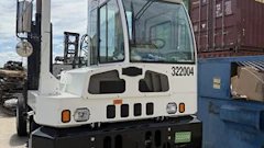 White industrial forklift with blue cabin parked in warehouse with shipping containers