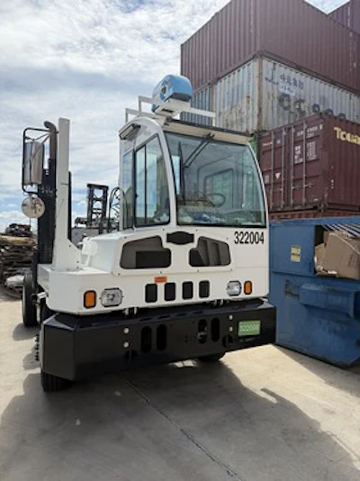 White industrial forklift with blue cabin parked in warehouse with shipping containers