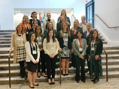 Group of professional women posing together on stairs at a corporate event or conference