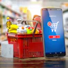 Mobile food delivery app interface on smartphone next to red shopping basket with groceries and receipt in supermarket setting