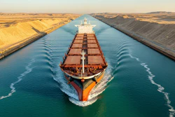 Large red and black cargo ship navigating through the Suez Canal with sandy desert banks on both sides