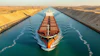Large red and black cargo ship navigating through the Suez Canal with sandy desert banks on both sides