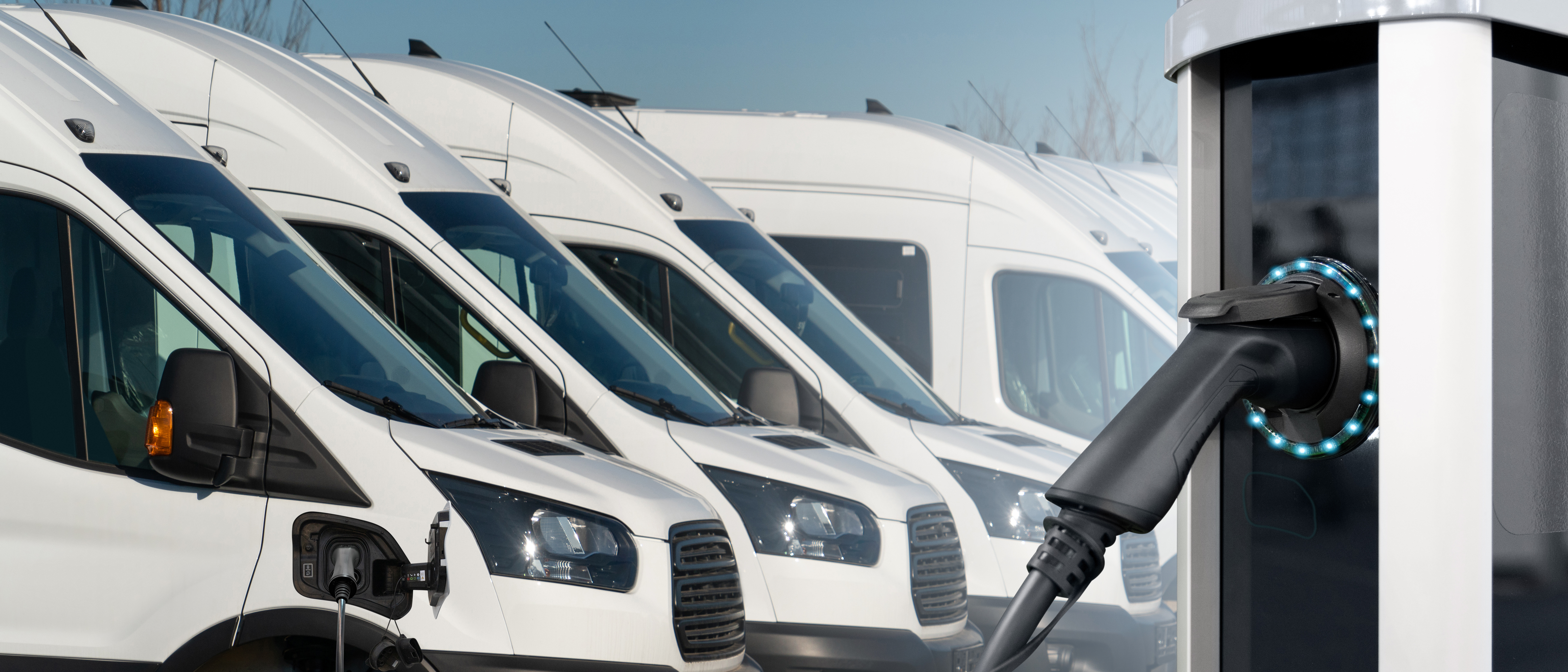Row of white commercial vans with electric vehicle charging station in foreground